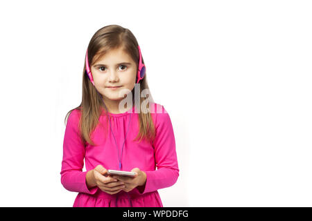 Kleine süße Mädchen Musik auf dem Smartphone im rosa Kleid und Kopfhörer. Auf den weißen Hintergrund isoliert. Konzept moderne Technologien, Kommunikation, Gadgets, etc. Stockfoto