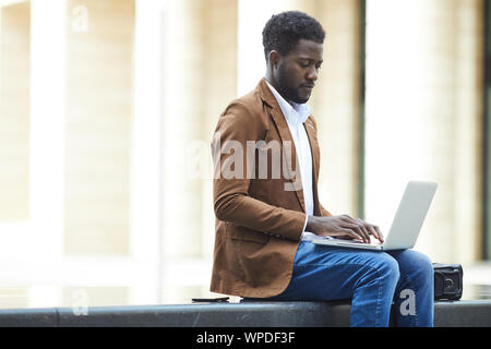 Seitenansicht Porträt der jungen Afrikaner - Mann mit Laptop im Freien während der Arbeit am Projekt im städtischen Raum einstellen, kopieren Stockfoto