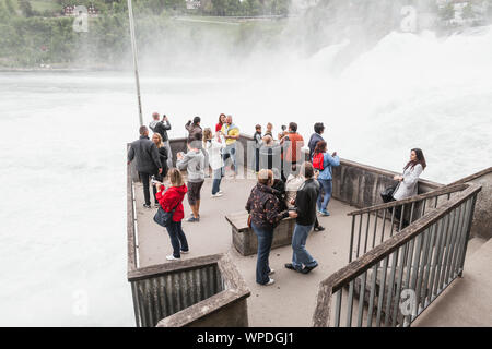 Rheinfall, Schweiz - 6. Mai 2017: Touristen sind auf den Aussichtspunkt am Rheinfall. Schnell fallende Wasser mit Schaum und Nebel auf einem Hintergrund Stockfoto