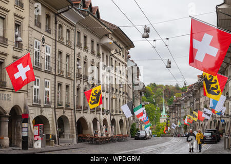 Bern, Schweiz - 7. Mai 2017: Street View der Kramgasse. Es ist eine der wichtigsten Straßen in der Altstadt von Bern. Menschen gehen unter bunten Flagge Stockfoto