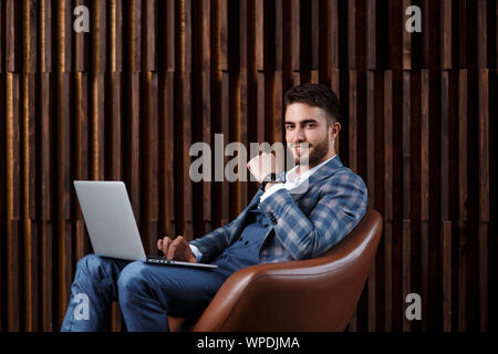 Junge erfolgreiche Unternehmer ist die Arbeit hinter einem Laptop, während in einem Loft Büro zu sitzen. bärtiger Mann, der an einem Notebook arbeitet. Stockfoto