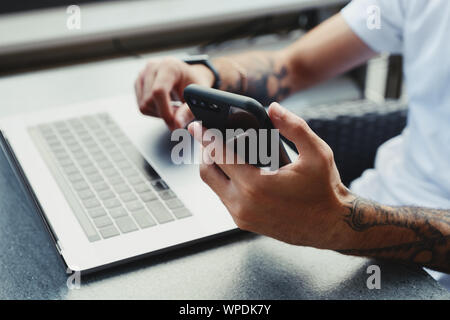 7/8 shot Sicht des Menschen, die von zu Hause aus arbeiten mit Smartphone und Laptop. Männliche lesen Sms auf Zelle Telefon, E-Mails, surfen Sie im Internet Stockfoto