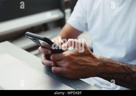 Nahaufnahme der Hand eines Mannes ist, Smartphone und Eingeben von Text im Bildschirm. Hipster Kerl Hände mit Tattoo mit Handy, Freiberufler lesen Stockfoto