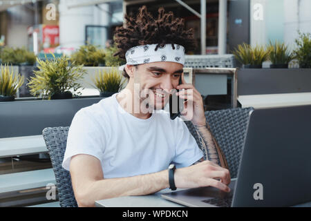 Fröhlicher junger Mann Freiberufler mit guten Nachrichten Gespräch am Handy zufrieden, glücklich hipster Kerl mit online abgeschlossen Projekt begeistert. Dist. Stockfoto