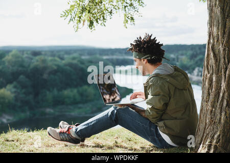 International Student mit Laptop im Freien in den öffentlichen Park konzentriert, suchen Informationen für e-learning, Hausaufgaben Aufgabe. Online cou Stockfoto