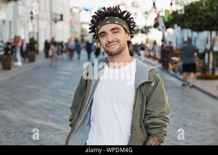 Überzeugter Kerl mit Dreadlocks Frisur, Nahaufnahme, Porträt, Straße Foto, urbanen Stil. Junge schöne Bart Mann verkleidet stilvolle legere Kleidung, Weiß Stockfoto