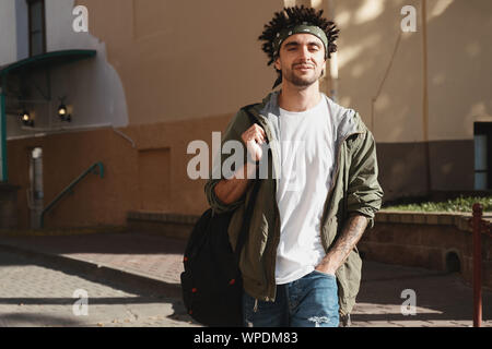 Gut aussehender bärtiger junger Mann mit Dreadlocks Frisur gekleidet modische Kleidung zu Fuß in der Stadt. Herbst Fashion Outfit, Outdoor Portrait, Urba Stockfoto