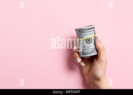 Blick von oben auf die weibliche Hand mit einem Pack von gewalzten Geld auf farbigen Hintergrund. Hundert Dollar. Business Konzept mit leeren Raum für Ihr Design. Stockfoto