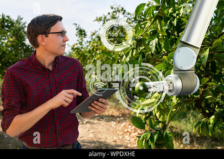 Bauer steuert Roboterarm mit einer Tablette. Smart Farming und digitale Transformation in der Landwirtschaft Stockfoto