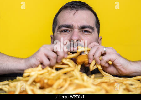 Essen der Trödelnahrung Ernährung und diätetischen Gesundheit Problem Konzept. Junger Mann essen mit beiden Händen eine sehr große Menge ungesundes fast food. Diät Versuchung r Stockfoto