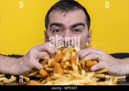 Essen der Trödelnahrung Ernährung und diätetischen Gesundheit Problem Konzept. Junger Mann essen mit beiden Händen eine sehr große Menge ungesundes fast food. Diät Versuchung r Stockfoto