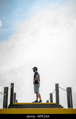 Low Angle ein bärtiger Mann mit dem Hut über eine Holztreppe, mit der bewölkte Himmel an einem Sommertag hat einen Hintergrund. Stockfoto