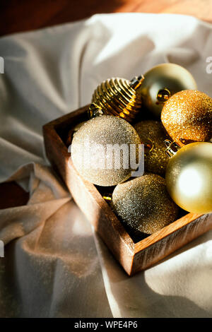 Weihnachten und neues Jahr Vorbereitung. Verschiedene vintage gold Weihnachtsdekoration Spielzeug oder Bälle in einer Holzkiste auf dem Boden. Festliche Stimmung Stockfoto