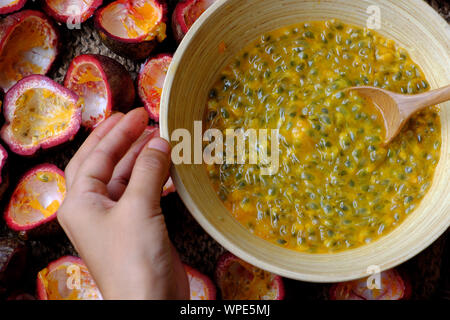 Ansicht von oben Frau hand Verarbeitung Passionsfrucht Passiflora edulis durch in die Hälfte geschnitten, mit einem Löffel Menschen weiche Fruchtfleisch und Samen im Inneren eine harte Schale, Schüssel Stockfoto