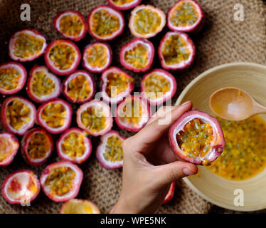 Ansicht von oben Frau hand Verarbeitung Passionsfrucht Passiflora edulis durch in die Hälfte geschnitten, mit einem Löffel Menschen weiche Fruchtfleisch und Samen im Inneren eine harte Schale, Schüssel Stockfoto