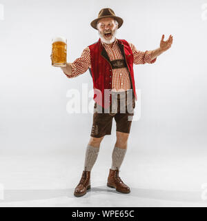 Portrait von Oktoberfest älterer Mann in Hut, das Tragen der traditionellen bayerischen Kleidung. Männliche in voller Länge Schuß an Studio auf weißem Hintergrund. Die Feier, Urlaub, festival Konzept. Bier trinkt. Stockfoto