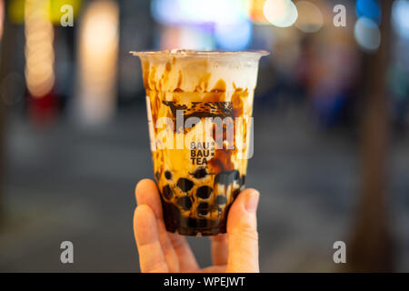 Hand mit Plastik Tasse schwarzen Zucker Milch Tee (Bubble Tea) mit verschwommenen bokeh Hintergrund (Bau Bau Tee) Stockfoto