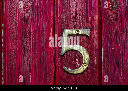 Hausnummer 5 auf einem alten roten Holztür Stockfoto