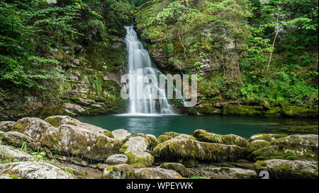Eine lange Belichtung Foto von einer schönen Wasser fallen über bemoosten Felsen in einen sauberen und klaren Bergsee. Von grünen Bäumen und Pflanzen umgeben Stockfoto