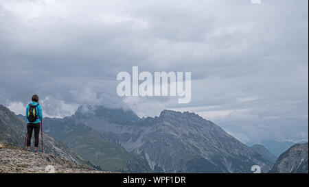 Eine einsame weibliche Wanderer blickt auf einige hochalpinen Berge und das Tal. Sturmwolken über den hohen Gipfeln, wie Sie denkt über die Aussicht auf das Tal. Stockfoto