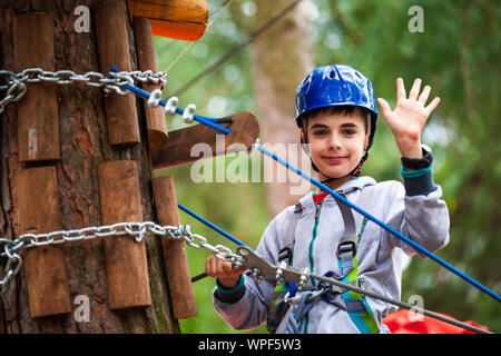 Junge Klettern über Hindernisse im Seil. Kind im Wald Abenteuer Park. Kinder klettern auf hohem Seil Trail. Agilität und Klettern outdoor Amusement cente Stockfoto