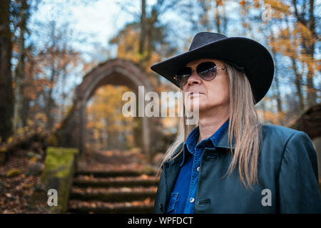 Portrait eines älteren langhaarigen Mann, Sonnenbrille und Hut im Wald auf düsteren Herbst Tag Stockfoto