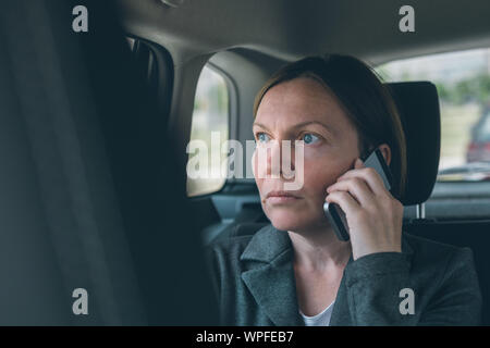 Zweifelnd Geschäftsfrau Gespräch am Handy auf dem Rücksitz, Wirtschaft in Bewegung Konzept. Elegante nach kaukasischen weibliche Person mit Smartphone Stockfoto