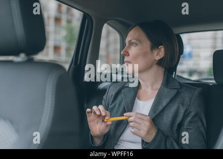 Geschäftsfrau warten an dem Auto Rücksitz und Spielen mit Bleistift Angst zu überwinden
