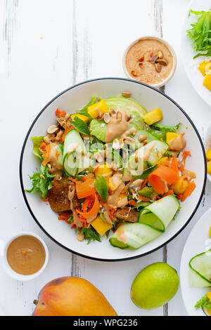 Gesund Sommer frischer Salat mit Mango, Avocado, Kalk und Tofu mit süßen Peanut butter Dressing weiße Holztisch Stockfoto