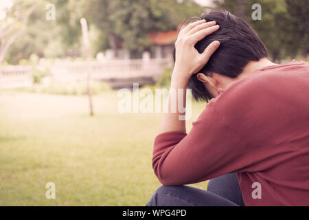Eine Person trägt ein rotes Hemd, greift sich bei Sonnenuntergang mit Stress im Garten den Kopf. Psychische Gesundheit, Depression Konzept. Stockfoto
