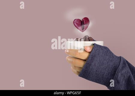 Die Hände einer Frau in einem Pullover mit einem Glas Kaffee Bohnen und rosa Herzen Kaffeebohne schwimmt über das Glas, Valentinstag und liebe Konzept. Stockfoto