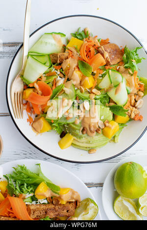 Gesund Sommer frischer Salat mit Mango, Avocado, Kalk und Tofu mit süßen Peanut butter Dressing weiße Holztisch Stockfoto