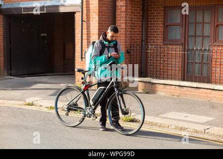 Deliveroo Radfahrer mit seinem mobilen Gerät entweder die Adresse einer Mahlzeit zum Mitnehmen Lieferung oder Details des nächsten Gerichte zum Mitnehmen bestellen zu sammeln. Großbritannien (113) Stockfoto