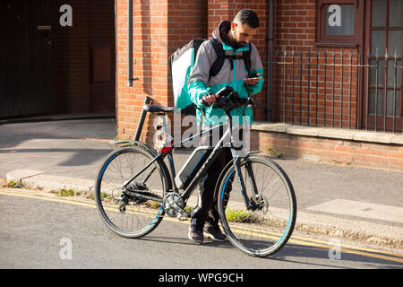 Deliveroo Radfahrer mit seinem mobilen Gerät entweder die Adresse einer Mahlzeit zum Mitnehmen Lieferung oder Details des nächsten Gerichte zum Mitnehmen bestellen zu sammeln. Großbritannien (113) Stockfoto