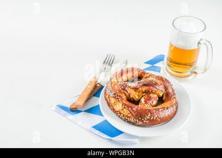 Oktoberfest festliche Besteck mit mit einem traditionellen karierten Tischdecken, Teller, Brezel, Gabel, Messer und ein Glas Bier. Hintergrund für Restor Stockfoto