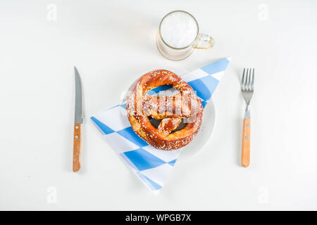 Oktoberfest festliche Besteck mit mit einem traditionellen karierten Tischdecken, Teller, Brezel, Gabel, Messer und ein Glas Bier. Hintergrund für Restor Stockfoto