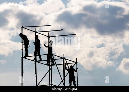 Bauarbeiter auf Gerüsten. Silhouetten, die Arbeiten auf der Baustelle gegen den blauen Himmel mit weißen Wolken Stockfoto