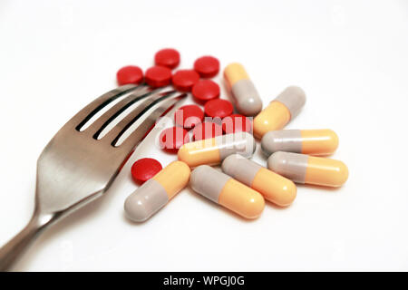 Pillen und Kapseln mit Gabel auf weiße Platte. Konzept der Schlankheitskur, Diätpillen, gesunde Ernährung, Vitamine, angereicherte Lebensmittel Stockfoto