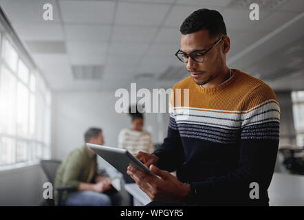 Junge smart Geschäftsmann in Freizeitkleidung beschäftigt sich mit digitalen Tablet im Büro konzentriert Stockfoto