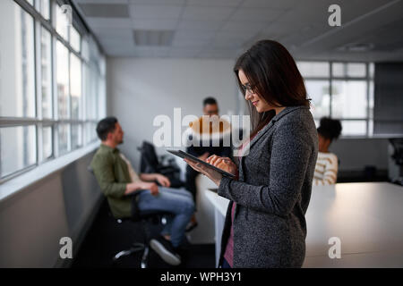 Lächelnden jungen Geschäftsfrau mit digitalen tablet, während Kollege im Hintergrund im Büro Stockfoto