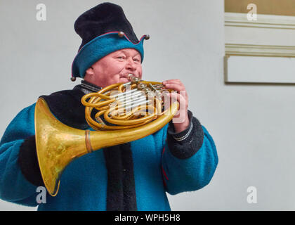 Dresden, Deutschland, 14. Dezember, 2018: Horn Gebläse in einem historischen blauen Kleid spielt auf dem alten Horn im Freien vor der weißen Wand Stockfoto