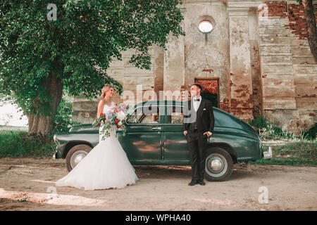 Glückliche Brautpaar steht neben einem stilvollen Auto während der Wanderung Stockfoto