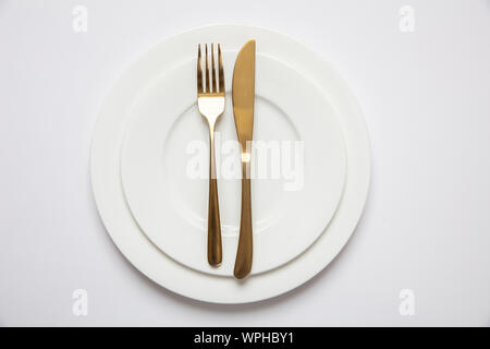 Tabelle mit Gold und Weiß, formale Abendessen. Golden Messer und Gabel auf weißem Geschirr isoliert, weißer Hintergrund, Ansicht von oben Stockfoto