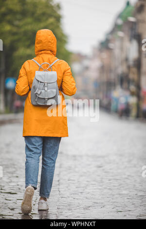 Frau im gelben Regenmantel zu Fuß durch die Straßen der Stadt unter Regen Stockfoto