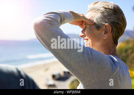 Seitenansicht der lächelnden älteren Frau Abschirmung Augen gegen Strand Stockfoto