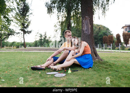 Tausendjährige Paar im Gras sitzen nach dem spielen Federball im Park Stockfoto