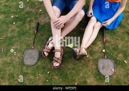 Tausendjährige Paar im Gras sitzen nach dem spielen Federball im Park Stockfoto