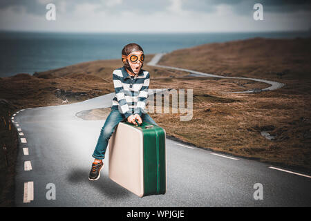 Kind gekleidet wie ein Flieger auf einen Koffer stellt sich ein Abenteuer fliegen auf einem verloren gegangenen Weg zu leben Stockfoto