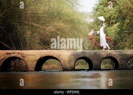 Frau mit Vietnam Kultur traditionelle Kleidung, Ao Dai und Fahrrad auf der Brücke Stockfoto