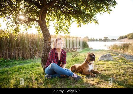 Jouful junge Mädchen ihren Hund streicheln, tragen Sport Kleidung, ihre Zeit und ihren Urlaub im sonnigen Park genießen. Stockfoto